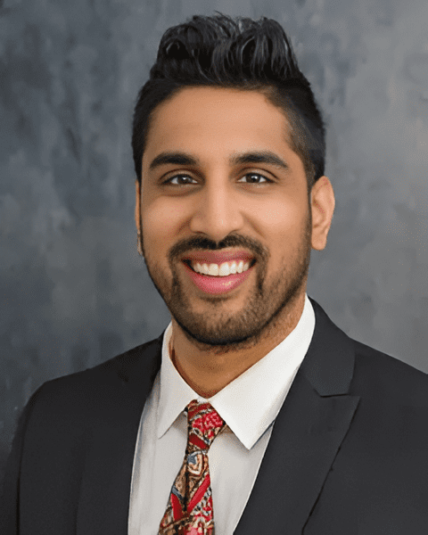 Expert orthopedic rehabilitation specialist Dr. Jason Kaushik smiling in a black suit and red tie