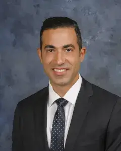 Expert orthopedic spine surgeon Dr. Siamak Yasmeh smiling in a black suit and slate tie