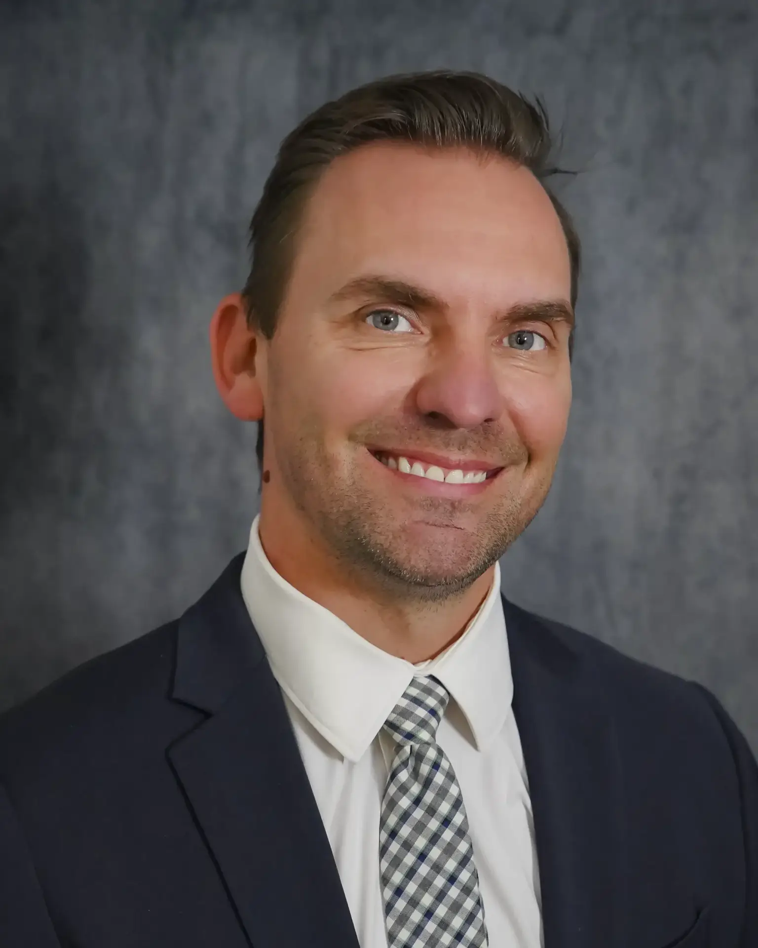 Expert orthopedic surgeon Dr. Matthew Longacre smiling in a navy suit and white and blue patterned tie