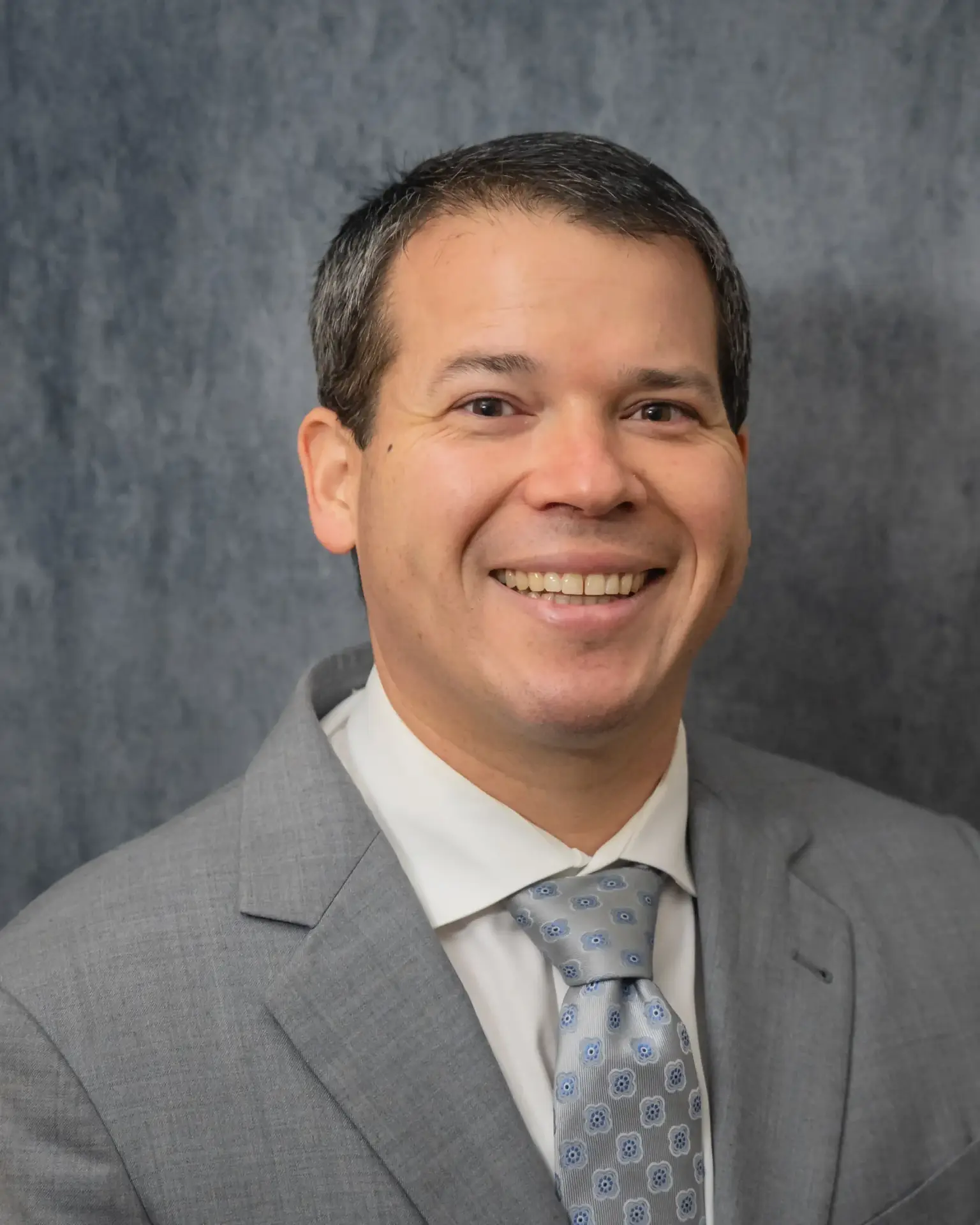 Expert orthopedic surgeon Dr. David Barba smiling in a gray suit and tie