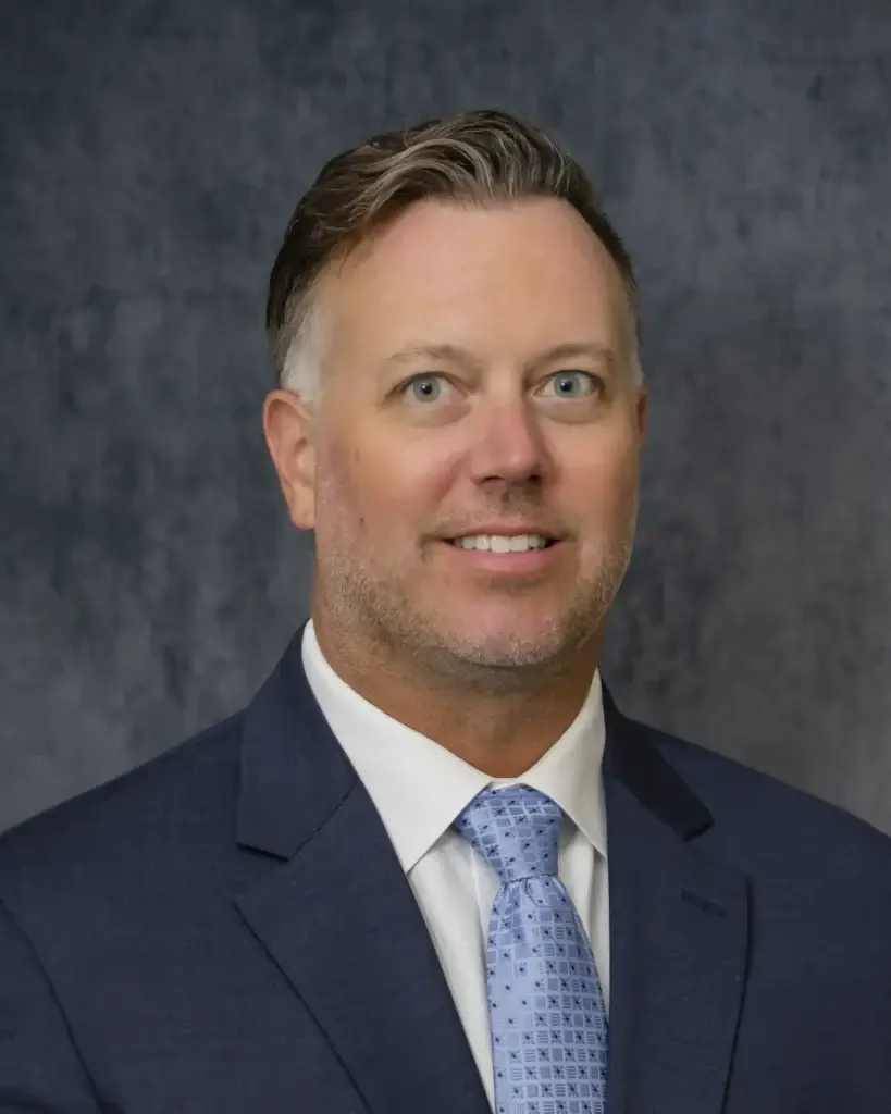 Expert orthopedic surgeon Dr. Kevin Pelton, MD smiling in a navy suit and light blue tie