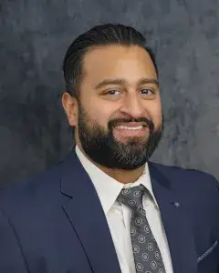 Expert orthopedic rehabilitation specialist Dr. Raj Desai smiling in a navy suit and silver tie