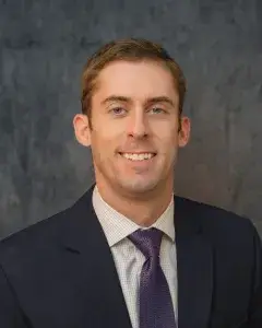 Expert orthopedic hand and wrist surgeon Dr. Brent Pickrell smiling in a navy suit and purple tie