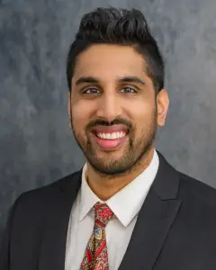 Expert orthopedic rehabilitation specialist Dr. Jason Kaushik smiling in a black suit and red tie